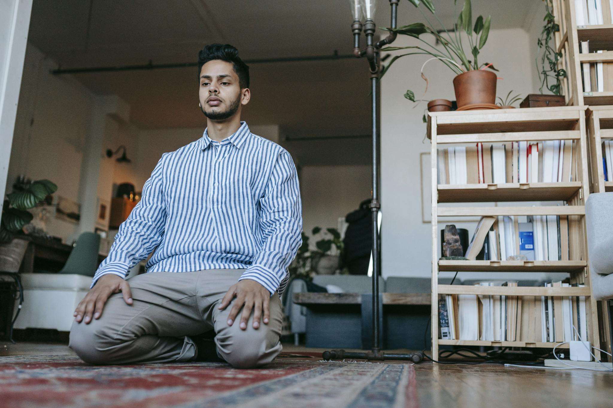 Man in Blue and White Striped Dress Shirt Sitting on Red and White Area Rug