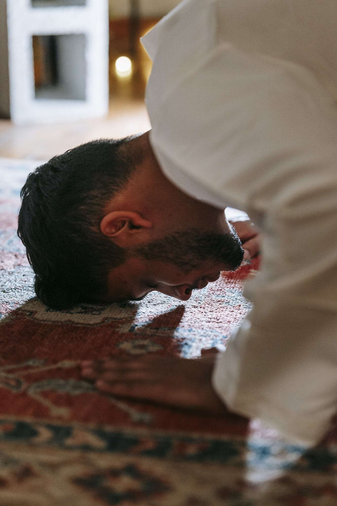 Man in White Thobe Bowing Down on Red and Blue Rug